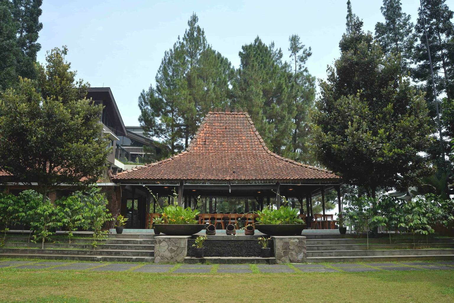 Pendopo beratap VANA SHANKARA dengan halaman rumput dan pepohonan di sekelilingnya