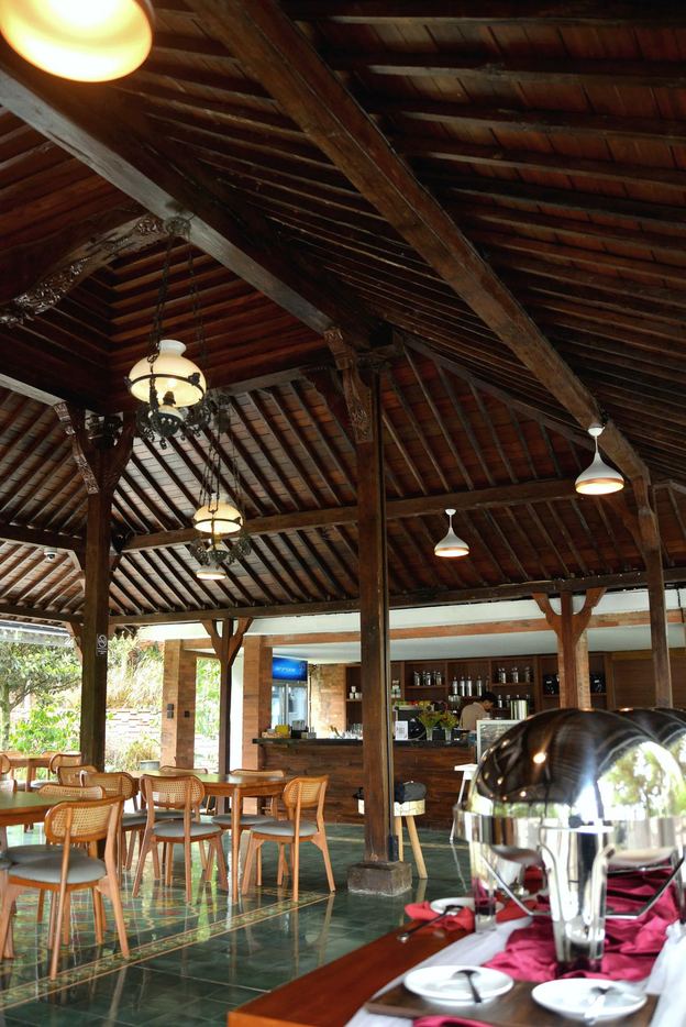 Ruang cafe VANA SHANKARA dengan meja kayu dan lampu gantung