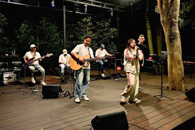 Gitaris dan penyanyi tampil di panggung VANA SHANKARA dengan lampu taman pada malam hari