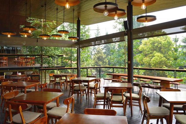Deretan meja kayu di resto terbuka VANA SHANKARA dengan latar hutan