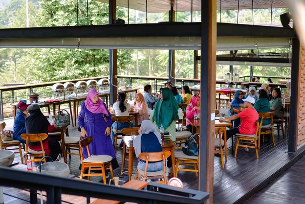 Ruang resto VANA SHANKARA dengan tamu duduk di meja kayu dan jendela kaca