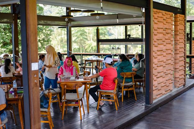 Ruang resto VANA SHANKARA dengan tamu duduk di meja kayu dan jendela kaca