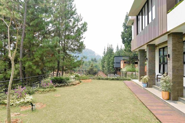 Halaman dalam vila VANA SHANKARA dengan rumput dan bangunan kayu, berlatar lembah