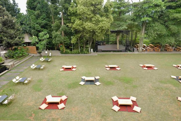 Halaman rumput VANA SHANKARA dengan meja piknik dan bean bag di bawah pepohonan