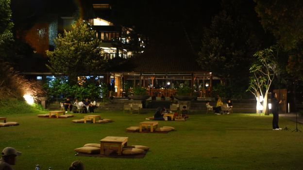 Halaman rumput VANA SHANKARA dengan lampu taman dan bangunan bercahaya pada malam hari