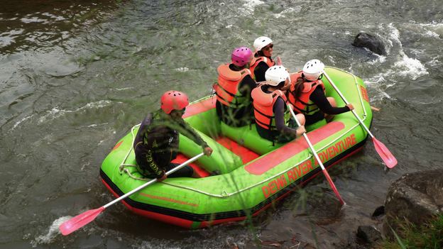 Peserta rafting di sungai dengan perahu karet hijau dan pelampung