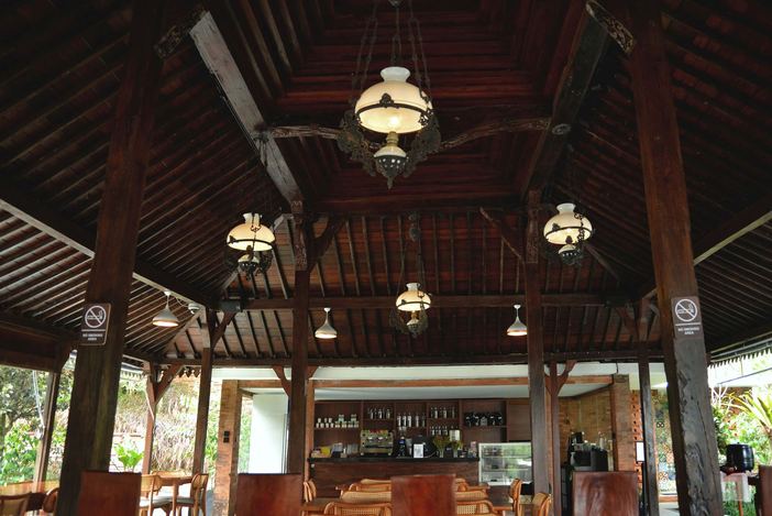 Ruang cafe VANA SHANKARA dengan meja kayu dan lampu gantung