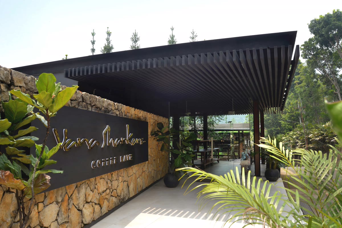 Papan nama Vana Shankara Coffee Rave di dinding batu di bawah kanopi kayu berbilah