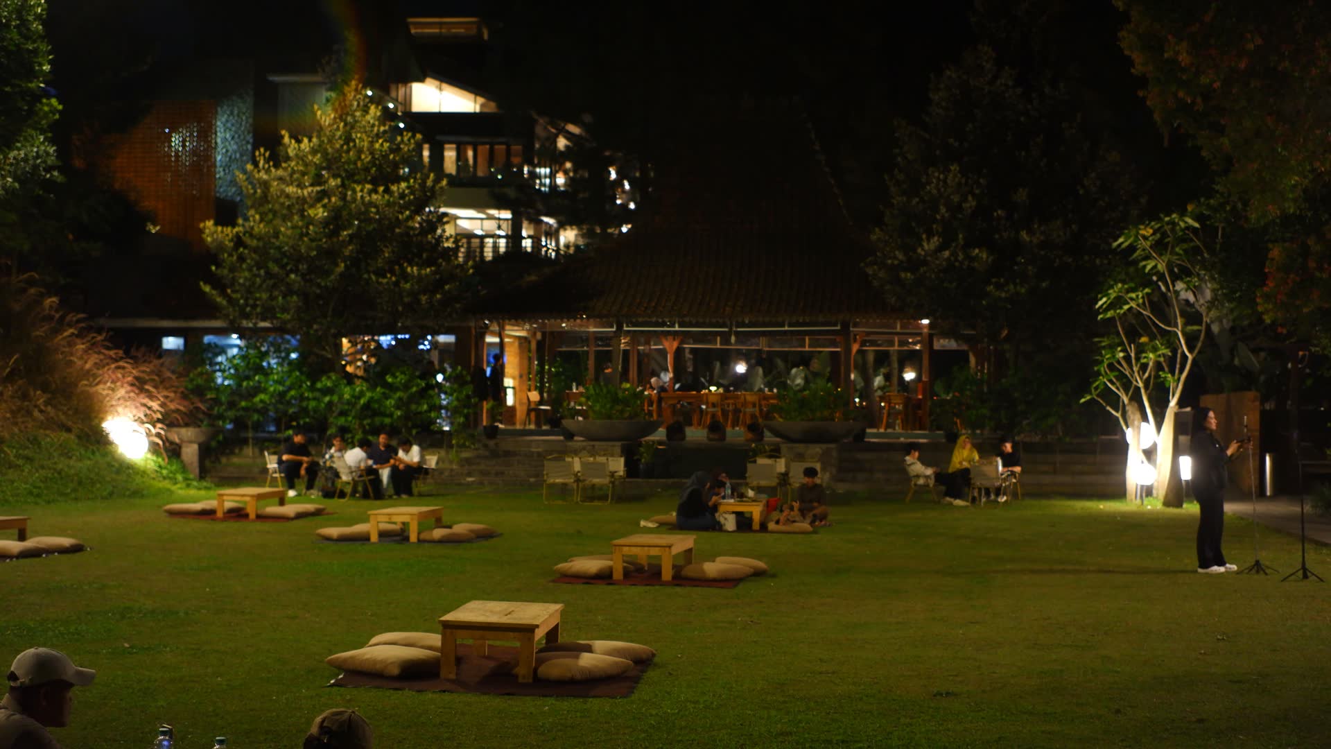 Halaman rumput VANA SHANKARA dengan lampu taman dan bangunan bercahaya pada malam hari