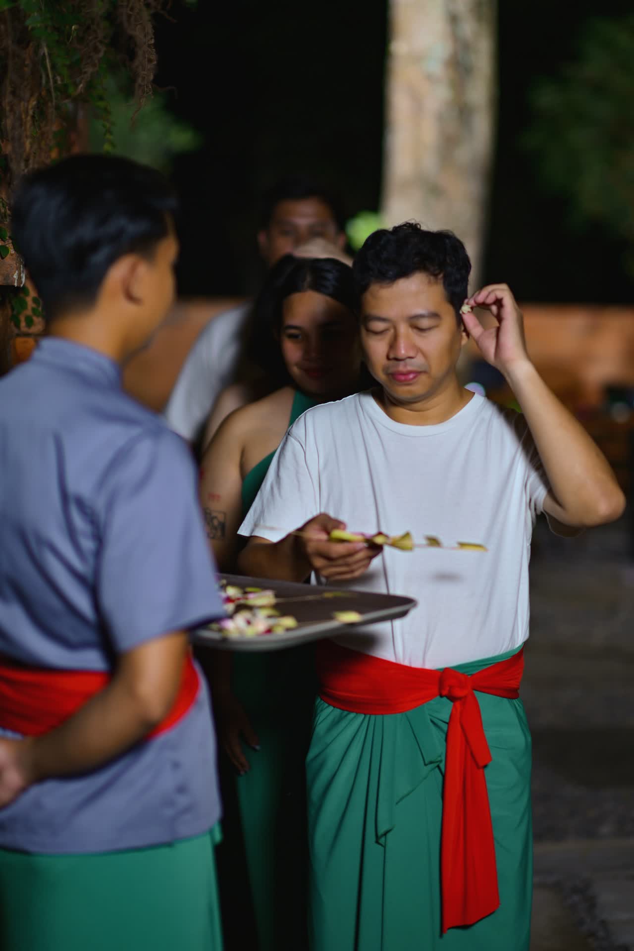 Tamu menerima bunga dari pemandu dalam prosesi melukat malam di VANA SHANKARA
